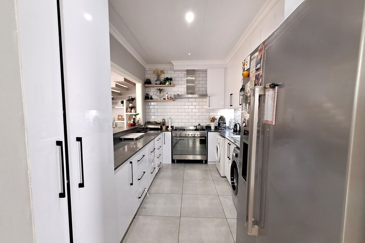 Modern galley-style kitchen featuring white cabinetry, subway tile backsplash, stainless steel gas range with extractor fan, and integrated laundry appliances.