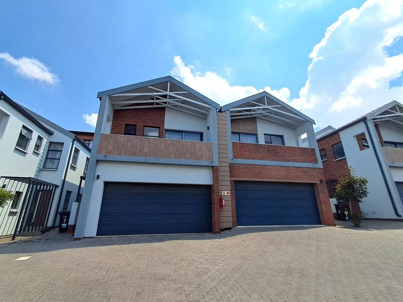 Front elevation of a modern townhouse complex featuring double garages, brick and plaster facade, and upper-level balconies with exposed roof trusses.
