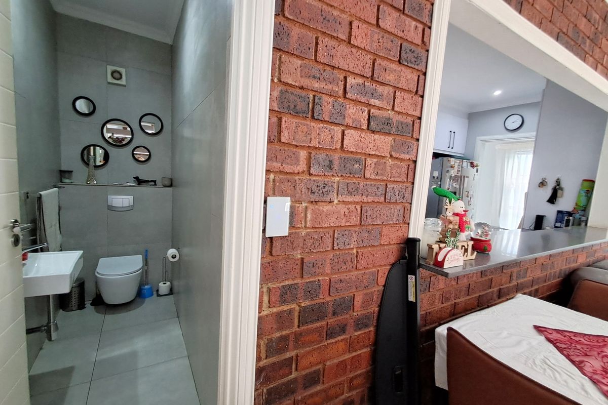 A view showing a modern guest bathroom with wall-hung toilet and basin, adjacent to a dining area featuring a brick feature wall and breakfast counter.