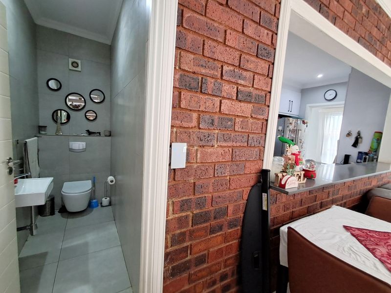 A view showing a modern guest bathroom with wall-hung toilet and basin, adjacent to a dining area featuring a brick feature wall and breakfast counter.