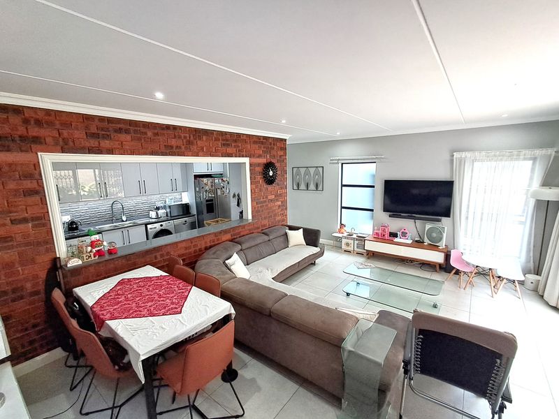 Spacious open-plan living and dining area featuring a brick feature wall and a large serving window connecting to the kitchen.
