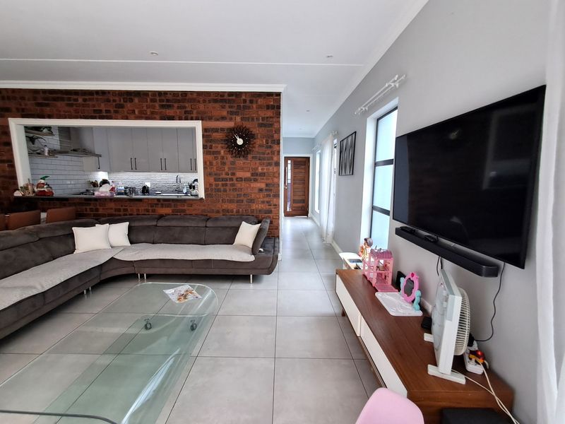 Open-plan living area featuring a striking exposed brick feature wall, large format floor tiles, and a convenient serving hatch connecting to the kitchen.