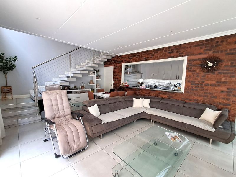 Open-plan living area featuring a modern floating staircase with stainless steel balustrades and an exposed brick feature wall overlooking the kitchen.