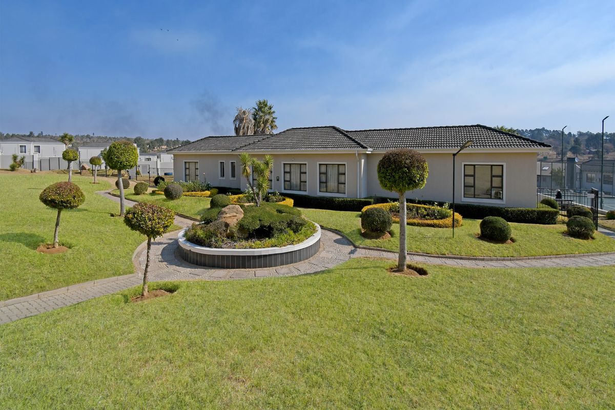 A well-maintained rear exterior view of the apartment building featuring a landscaped garden, paved pathways, and a stone feature.