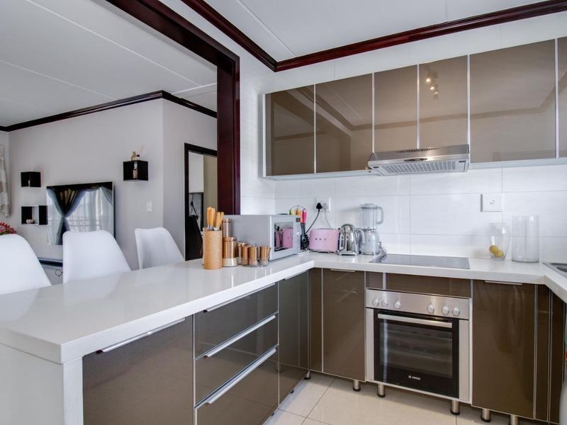 Modern kitchen featuring high-gloss cabinetry, stone countertops, integrated oven, and electric hob, seamlessly flowing into the adjacent living area.