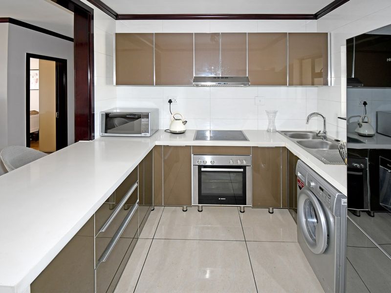 Modern kitchen featuring glossy cabinetry, stone countertops, integrated appliances, and tiled flooring, offering a clean and functional workspace.