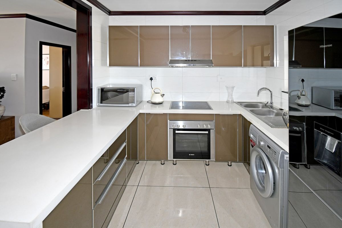 Modern kitchen featuring glossy cabinetry, stone countertops, integrated appliances, and tiled flooring, offering a clean and functional workspace.