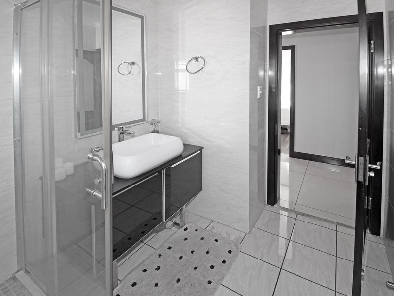 Modern bathroom featuring a glass shower enclosure, a sleek vessel sink with a vanity cabinet, and neutral wall and floor tiling.
