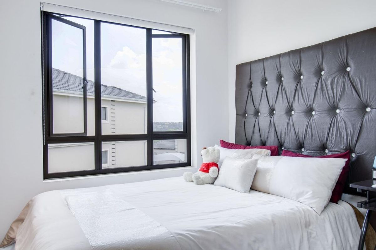 A bright and well-maintained bedroom featuring a large aluminium-framed window that allows for ample natural light.
