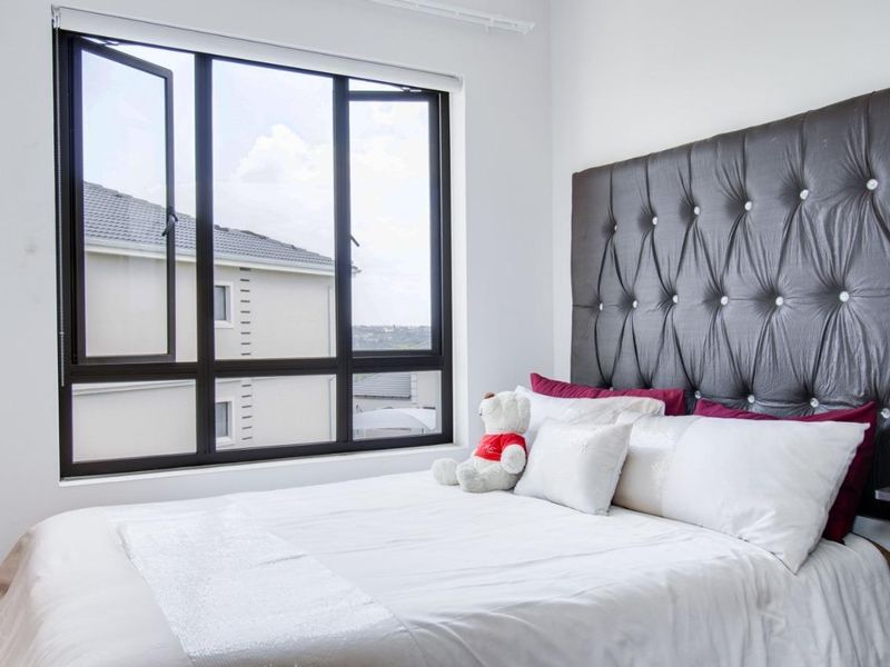 A bright and well-maintained bedroom featuring a large aluminium-framed window that allows for ample natural light.
