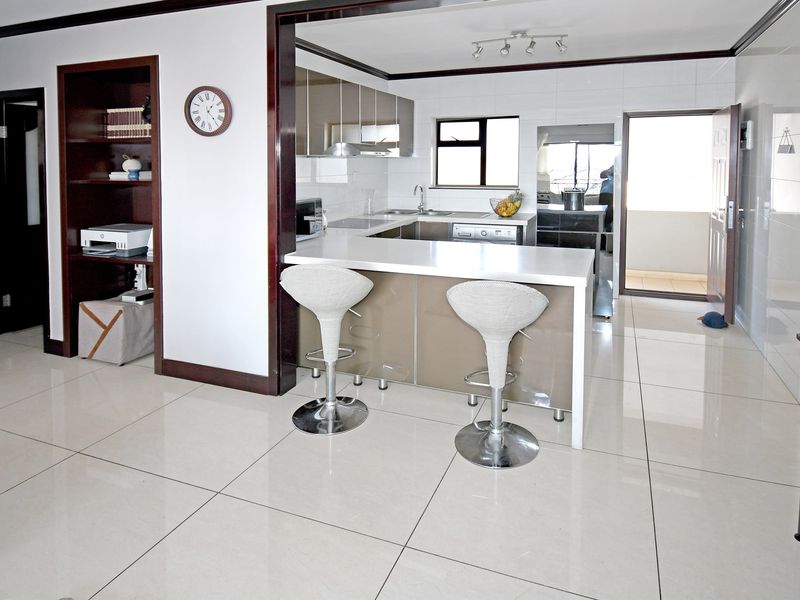 Modern open-plan kitchen featuring high-gloss cabinetry, stone countertops, and polished ceramic floor tiles, seamlessly connected to the living area.