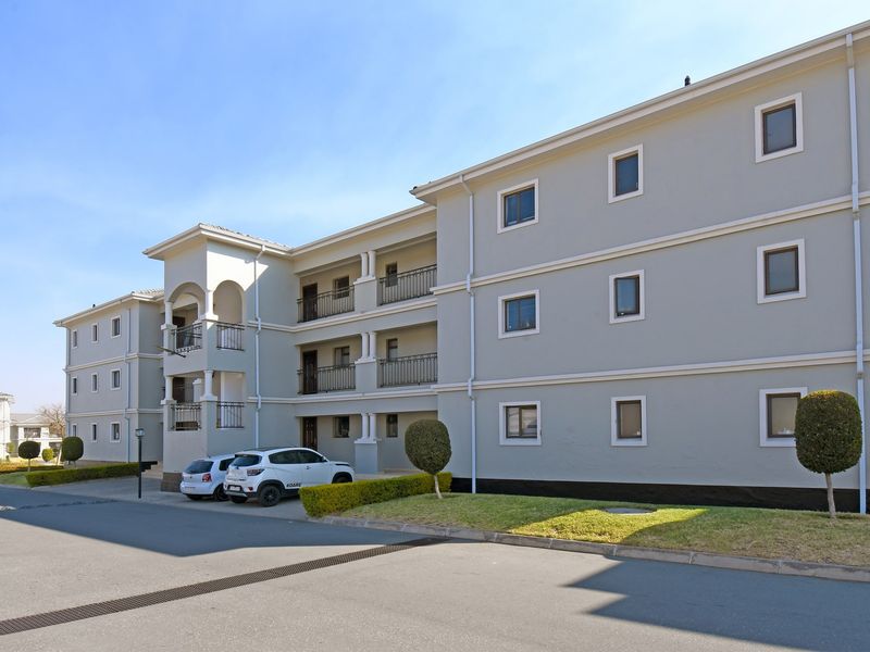 Exterior view of a multi-story apartment complex featuring balconies with wrought iron railings, paved driveway, and well-maintained landscaped garden areas.