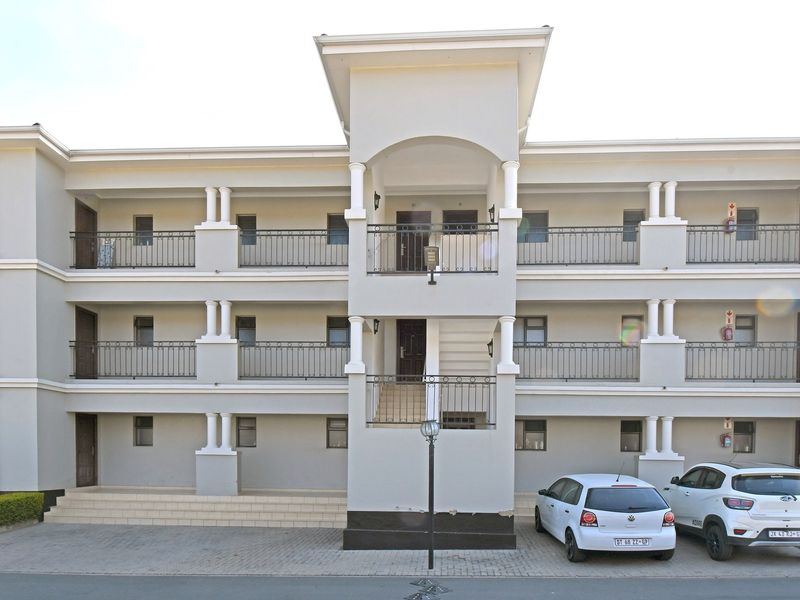 Front elevation of a multi-story apartment complex featuring a central staircase, wrought iron balcony railings, and paved parking area.