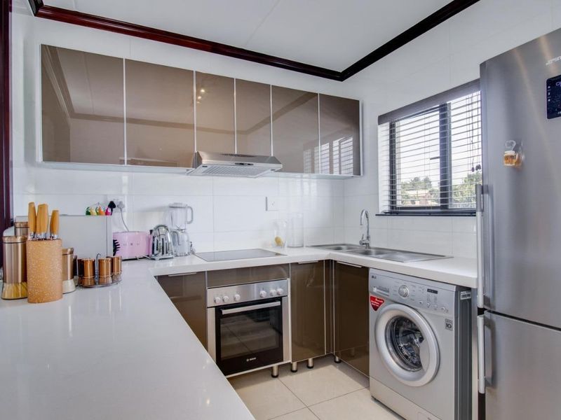 Modern kitchen featuring high-gloss cabinetry, quartz countertops, integrated appliances, and a tiled backsplash, offering a clean and functional cooking space.