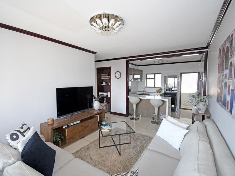 Open-plan living area featuring tiled floors, crown molding, and a functional kitchen with a breakfast island and built-in cabinetry.