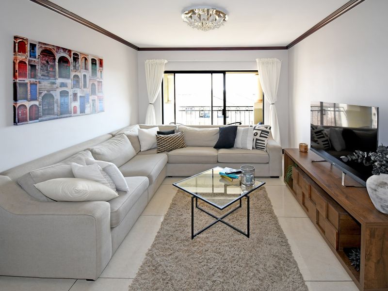 A well-maintained living room featuring tiled flooring, crown molding, and a sliding glass door leading to a balcony, providing ample natural light.