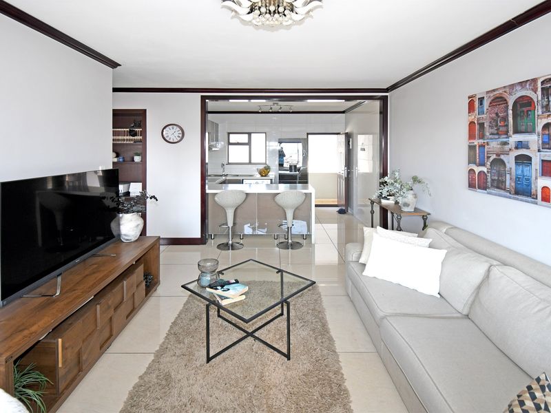 An open-plan living area featuring polished floor tiles, crown molding, and a seamless transition to a modern kitchen with a central island.