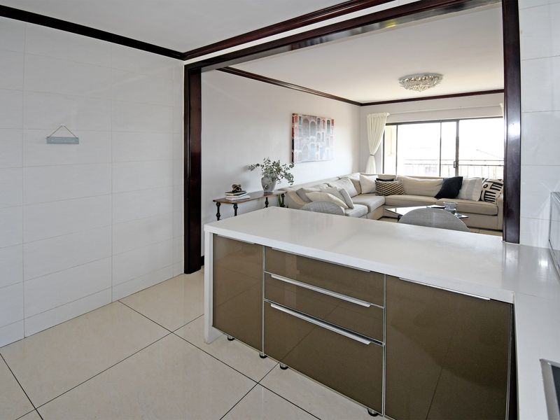 Open plan kitchen and living area featuring a modern kitchen island with stone countertops, glossy cabinetry, and large sliding doors leading to a balcony.
