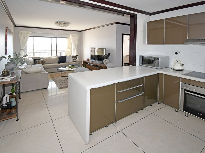 Modern open-plan living area featuring a sleek kitchen with high-gloss cabinetry, integrated appliances, and large porcelain floor tiles leading to a balcony.