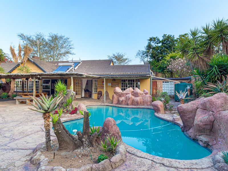 Outdoor entertainment area featuring a swimming pool with natural rock landscaping, a covered patio, and solar water heating system.