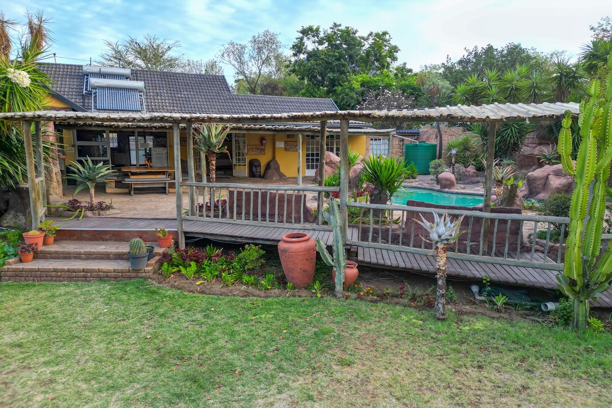 Rear exterior view featuring a covered wooden patio, swimming pool, landscaped garden, and solar water heating system on the roof.