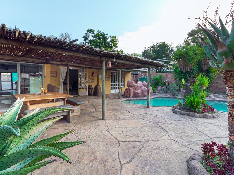 Covered outdoor patio area featuring a thatched roof, stone paving, and direct access to a swimming pool with decorative rock landscaping.
