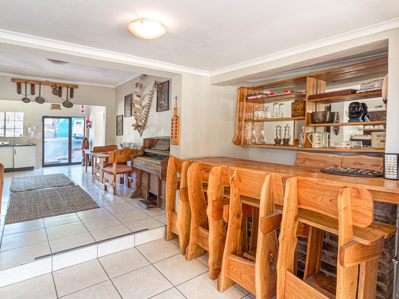 A rustic bar area featuring a built-in wooden counter, integrated shelving, and tiled flooring, with an adjacent view into a secondary kitchen space.