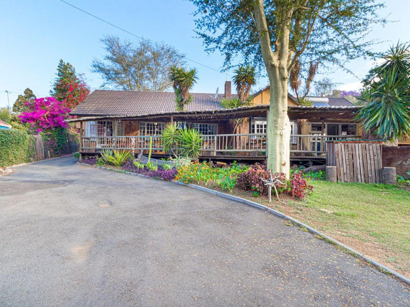 Front view of a house featuring a large timber deck, tiled roof, and an asphalt driveway surrounded by established garden beds.