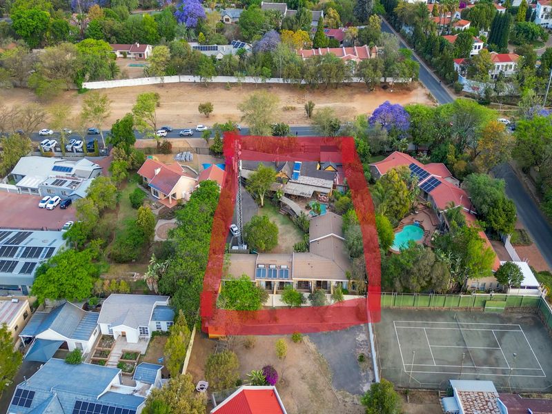 Aerial view of a residential property featuring a main house, swimming pool, and established garden within a suburban neighborhood setting.