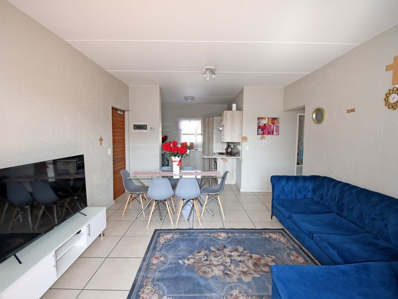 Open-plan living and dining area featuring tiled flooring and a compact kitchen with built-in cabinetry and integrated appliances.