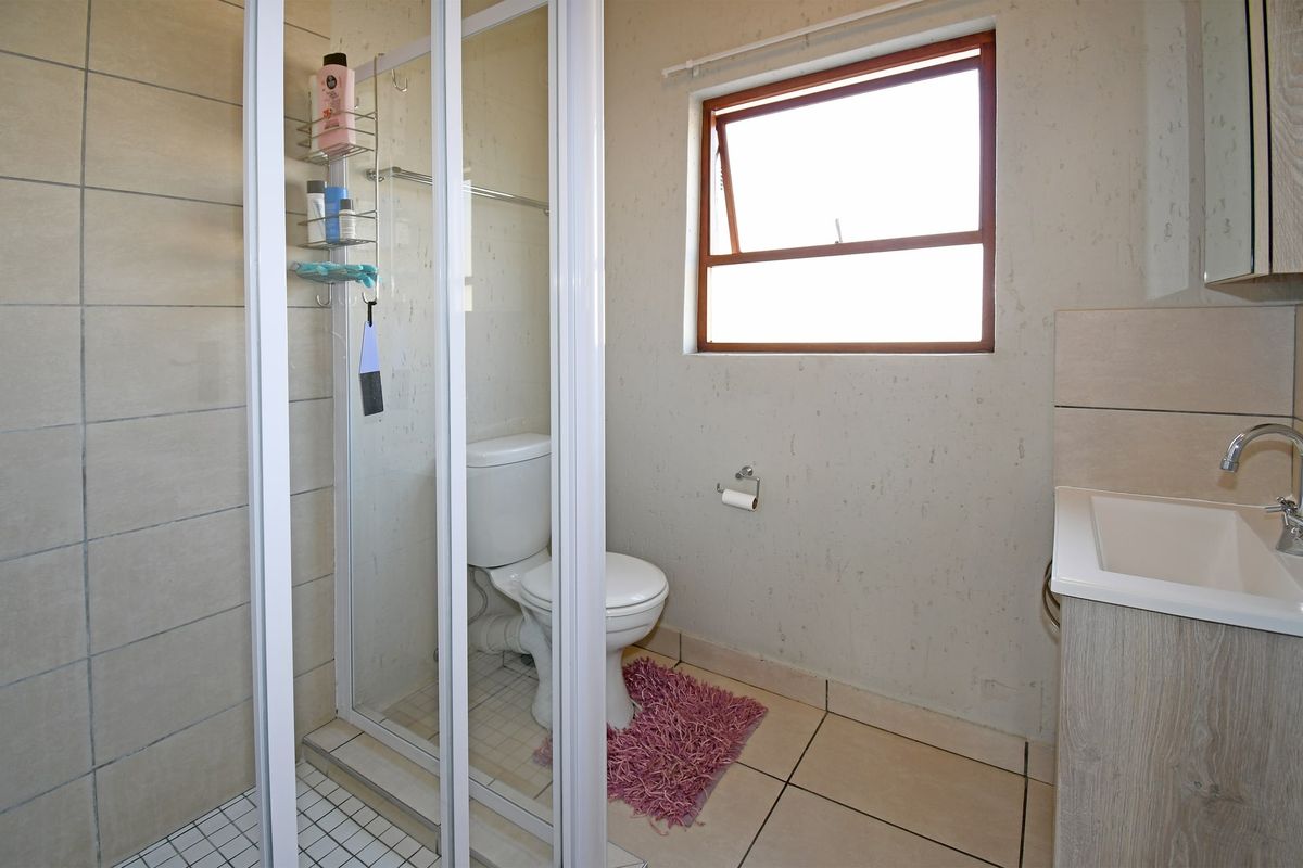 A functional bathroom featuring a shower enclosure, toilet, and vanity cabinet with a basin, finished with tiled flooring and walls.