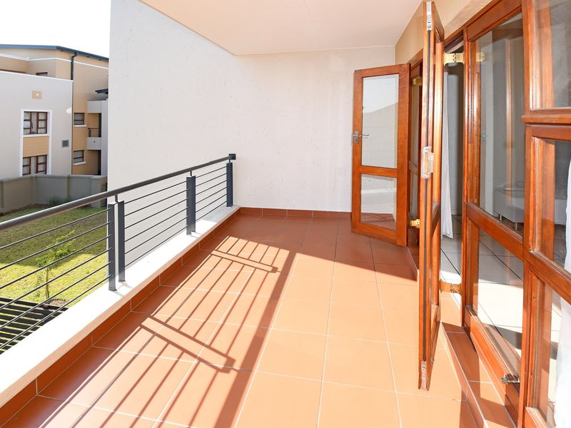 A spacious, tiled balcony featuring a metal balustrade and wooden-framed glass doors, offering an open outdoor area accessible from the interior.