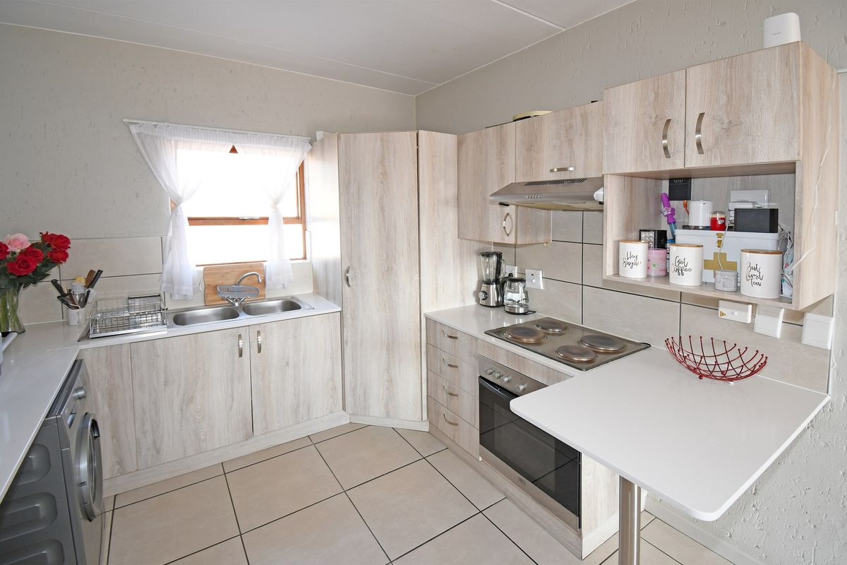 A functional kitchen featuring light wood-look cabinetry, a built-in oven and hob, double basin sink, and a convenient breakfast counter with tiled flooring.