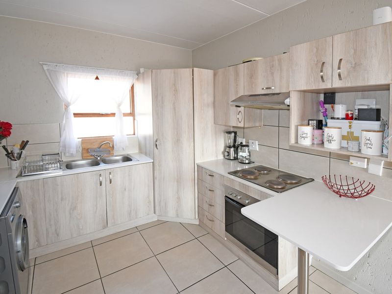 A functional kitchen featuring light wood-look cabinetry, a built-in oven and hob, double basin sink, and a convenient breakfast counter with tiled flooring.