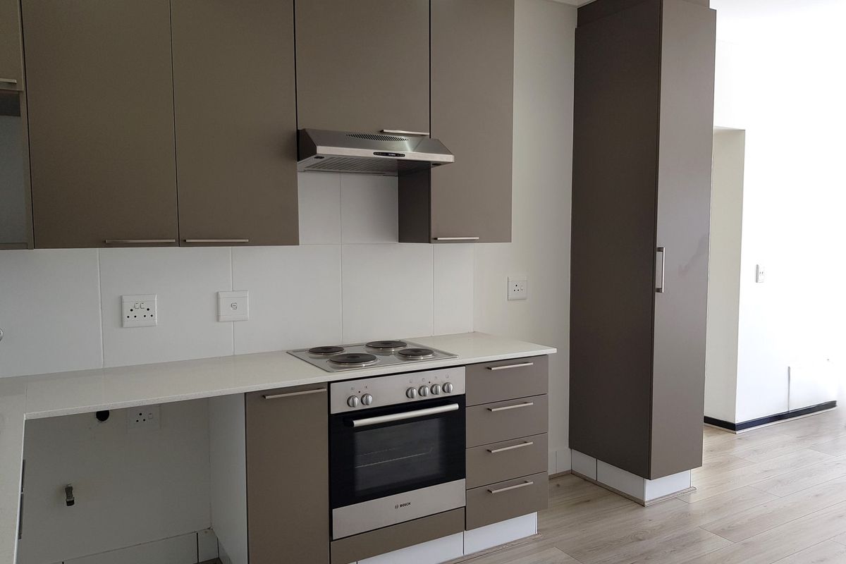 Modern kitchen featuring sleek taupe cabinetry, stone countertops, built-in oven, electric hob, and extractor fan, with light laminate flooring throughout.
