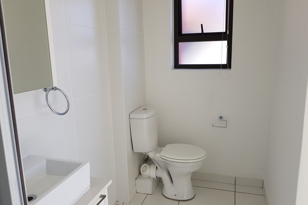 A clean and functional bathroom featuring a modern vanity basin, white tiled walls and flooring, and a private frosted window.