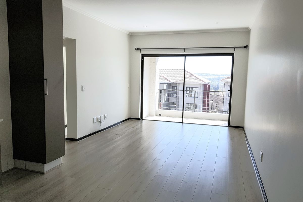 A bright, empty living room featuring modern laminate flooring, recessed lighting, and a large sliding glass door leading to a private balcony.