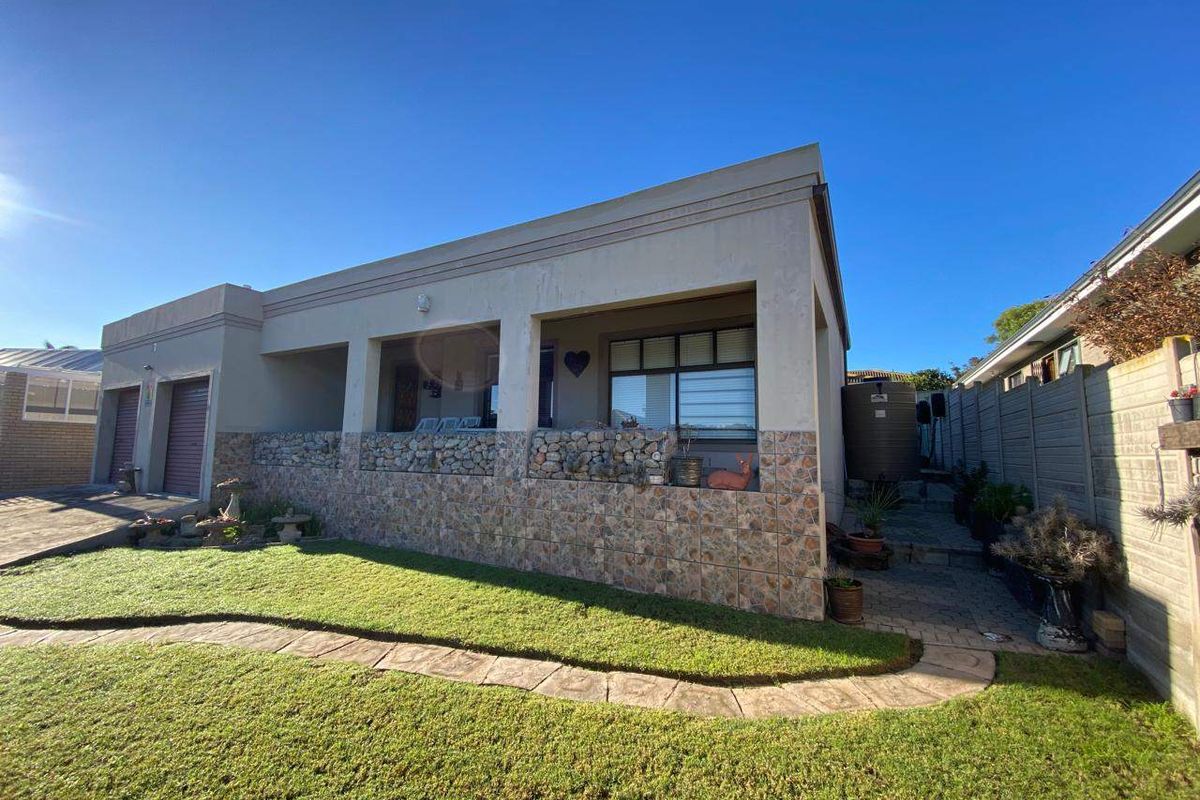 Rear view of the property featuring a covered patio with stone cladding, a paved walkway, a water tank, and a well-maintained lawn.