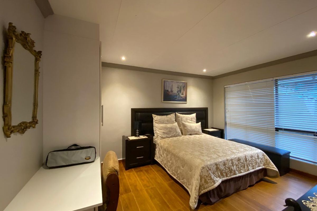 A well-maintained bedroom featuring laminate flooring, built-in cupboards, recessed downlighting, and large windows fitted with venetian blinds.