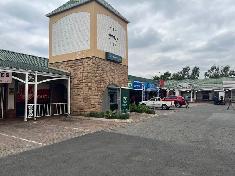 Exterior view of a commercial shopping center featuring a prominent clock tower, stone masonry detailing, and an integrated ATM kiosk.