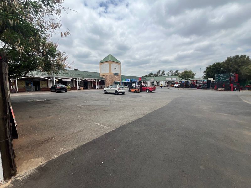 Exterior view of a commercial retail center featuring a central clock tower, covered walkways, and an expansive asphalt parking area.