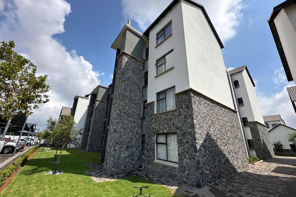 Exterior view of a multi-story apartment building featuring stone cladding, white rendered walls, and well-maintained surrounding lawn and paved pathways.