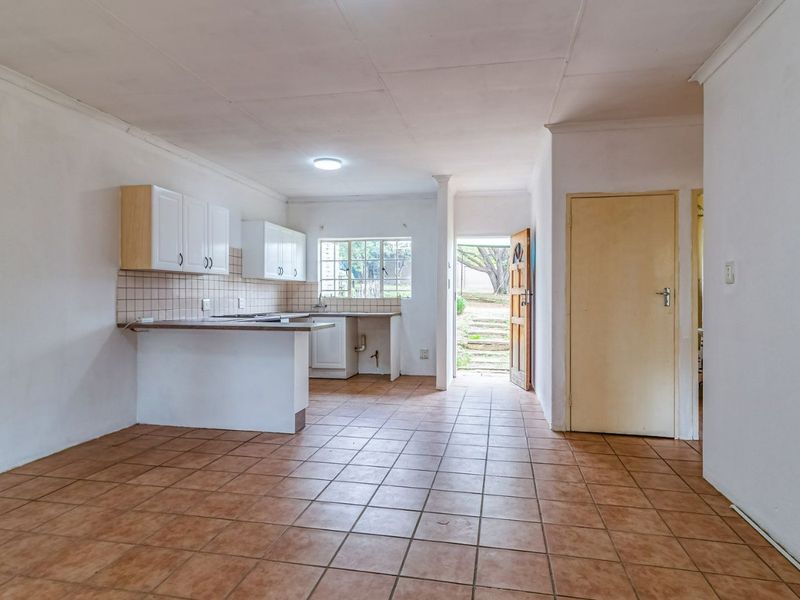 An open-plan kitchen and living area featuring tiled flooring, built-in cabinetry, and direct access to the exterior, offering a blank canvas for renovation.