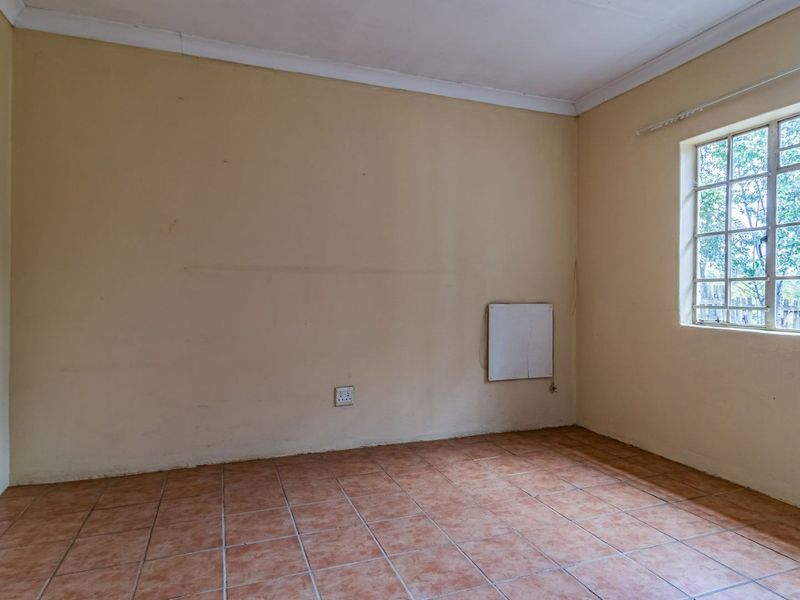 An empty bedroom featuring tiled flooring, a steel-framed window, and neutral wall finishes, providing a blank canvas for renovation or interior design.
