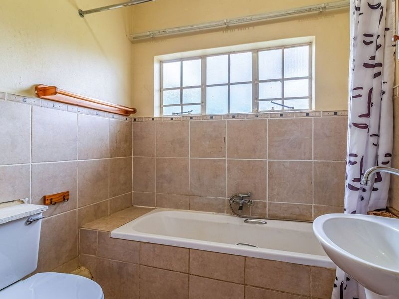 A functional bathroom featuring a built-in bathtub, pedestal washbasin, and tiled wall finishes, offering potential for modernization and aesthetic updates.