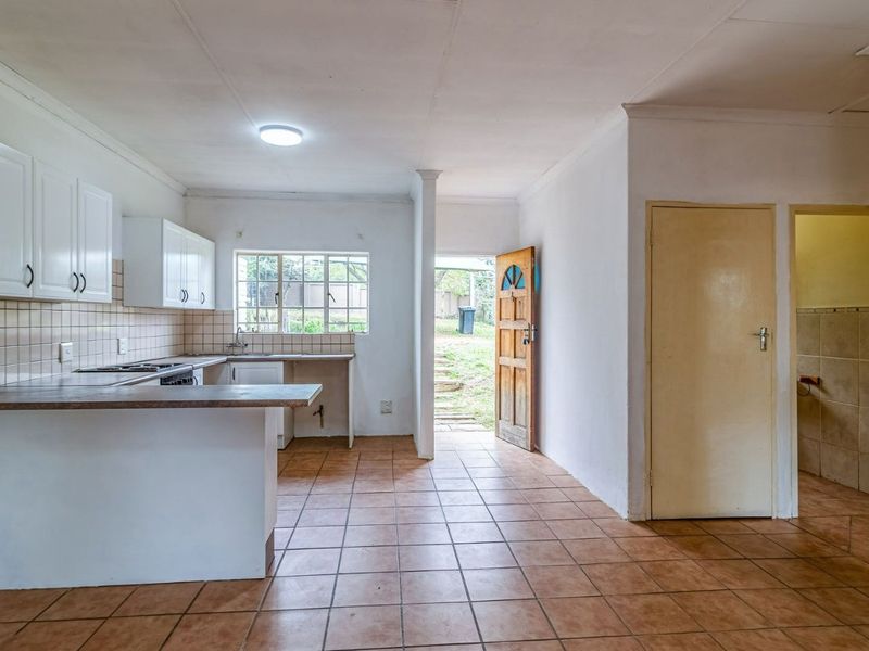A functional kitchen space featuring tiled flooring, built-in cabinetry, and a tiled backsplash, with direct access to the exterior.