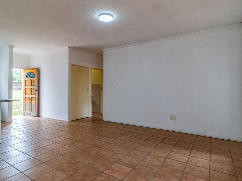 An open-plan living area featuring ceramic tile flooring, neutral walls, and direct access to the entrance and kitchen space.
