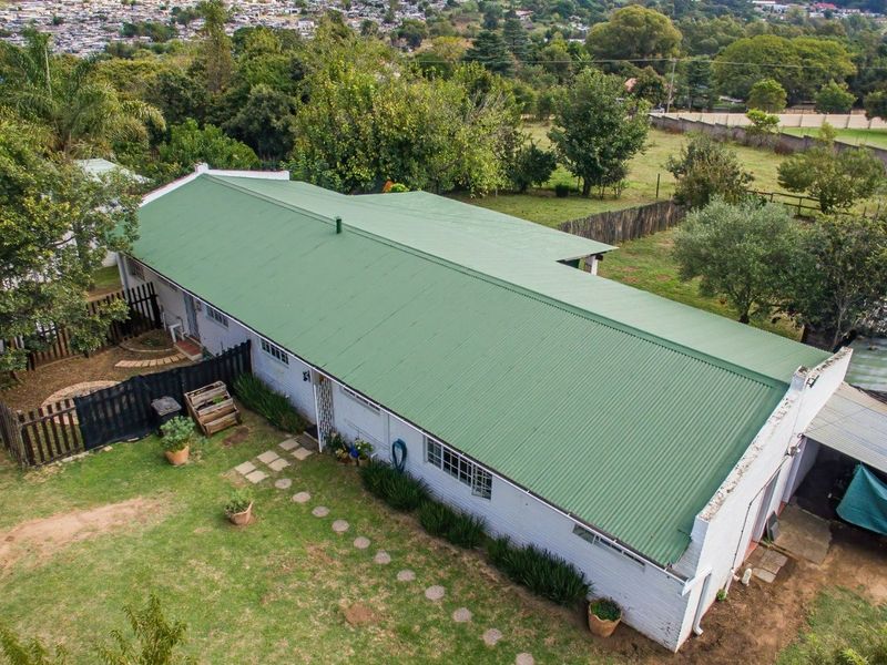 Aerial view of a commercial property featuring a large green corrugated metal roof, brick exterior walls, and surrounding garden space.