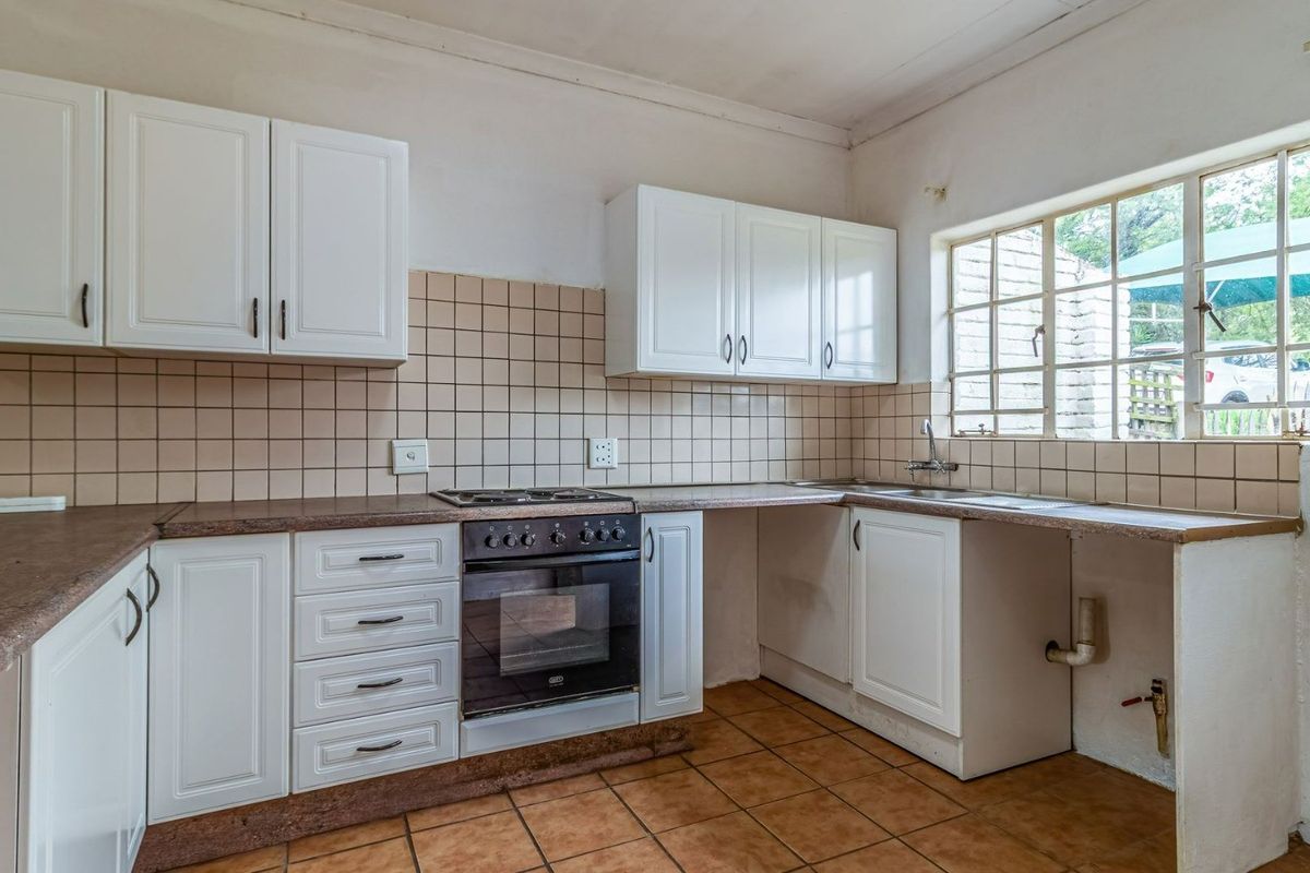 A functional kitchen featuring white cabinetry, a built-in oven with gas hob, tiled backsplash, and a stainless steel sink under a large window.