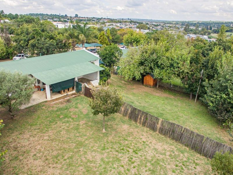 Aerial view of the property grounds featuring a building with a green metal roof, a covered patio area, and a spacious garden with fencing.